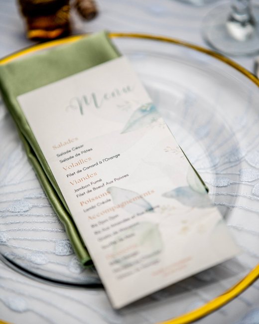 Menu de mariage posé sur une serviette verte, dans une assiette en verre bordée d'or